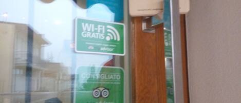 Una puerta de vidrio con varios letreros, incluyendo un símbolo de Wi-Fi, un letrero que indica Wi-Fi gratis y un letrero de TripAdvisor.