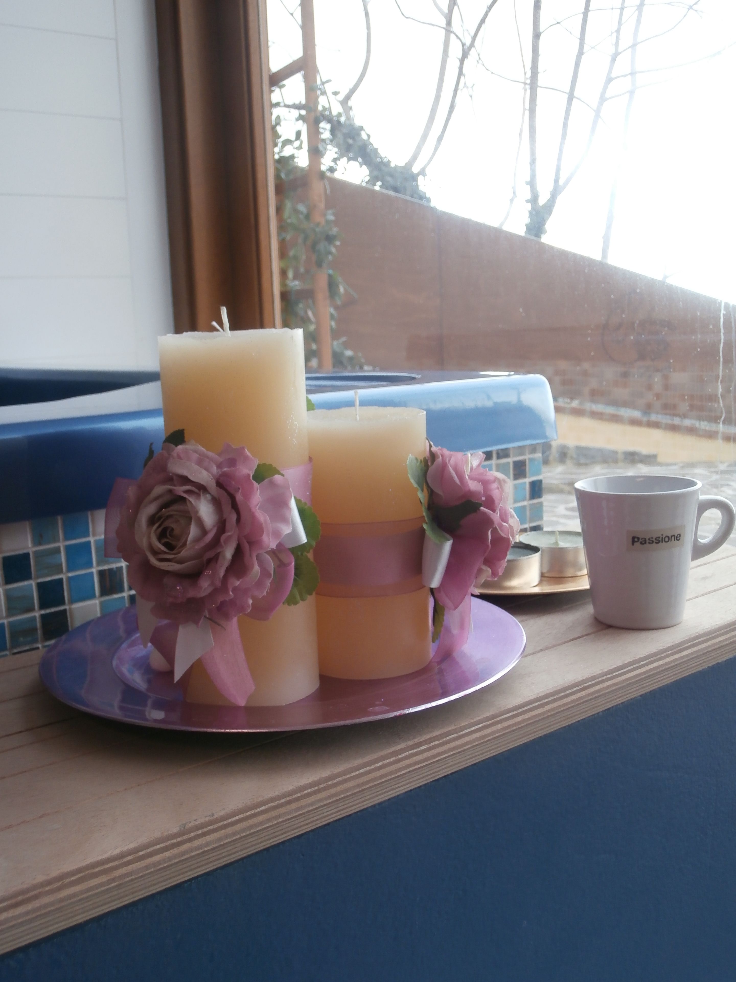 A candle arrangement with a white mug on a windowsill.