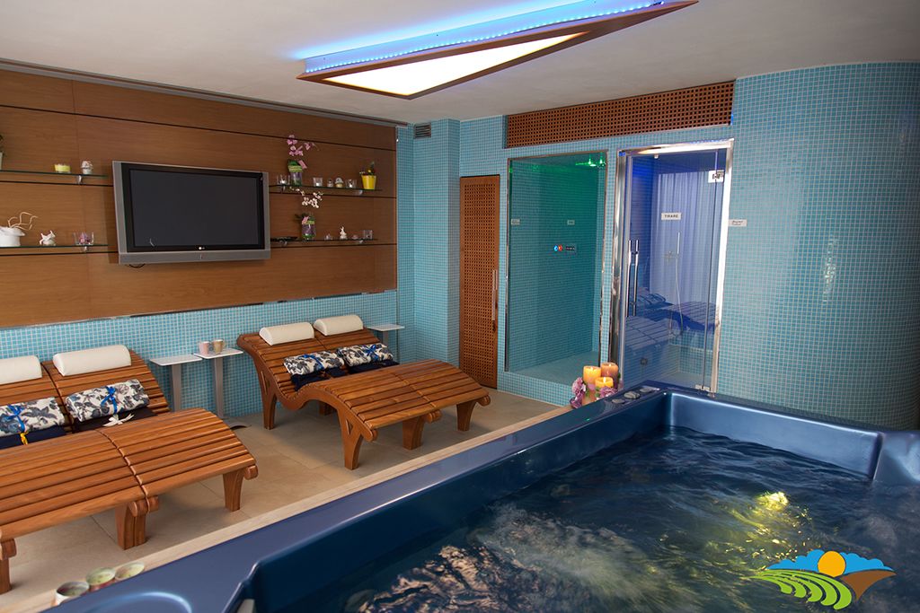 Un'area benessere con lettini in legno, una televisione e una vasca idromassaggio.