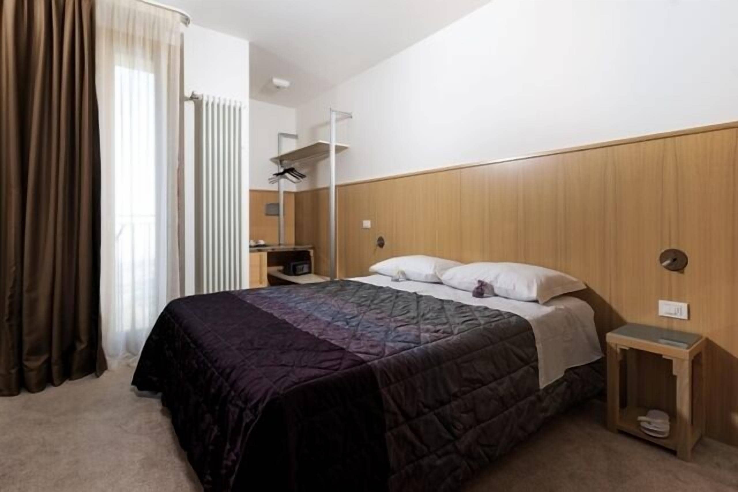 Un dormitorio con cama, cabecera de madera, mesita de noche y radiador.