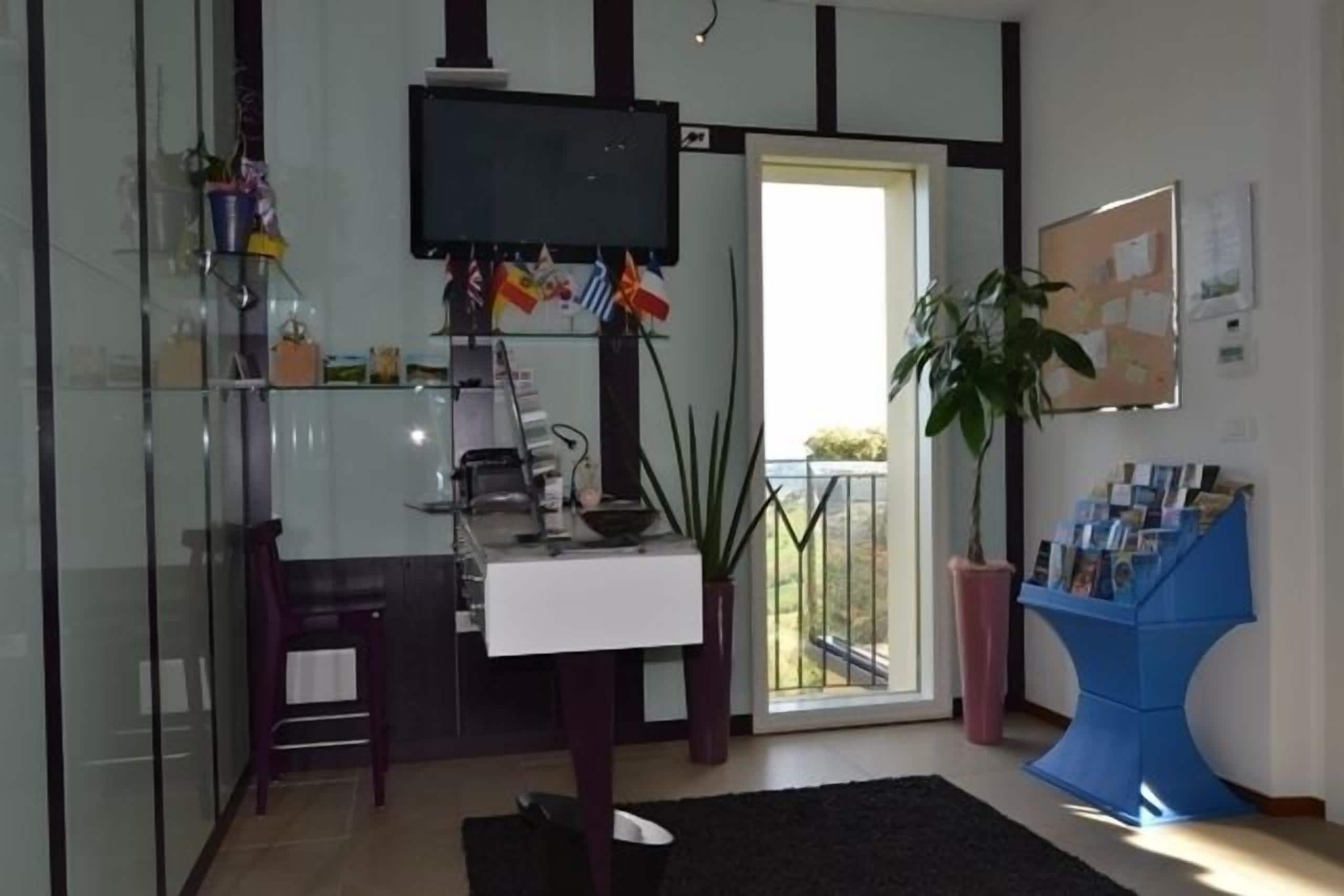 Una sala de estar moderna con un separador de vidrio, un televisor de pantalla plana, un escritorio con una computadora, una silla, una planta en maceta y un revistero azul.