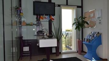 Una sala de estar moderna con un separador de vidrio, un televisor de pantalla plana, un escritorio con una computadora, una silla, una planta en maceta y un revistero azul.