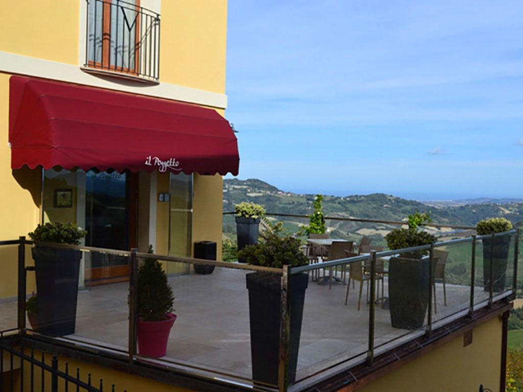 A balcony with a red awning, potted plants, and a view of the countryside.