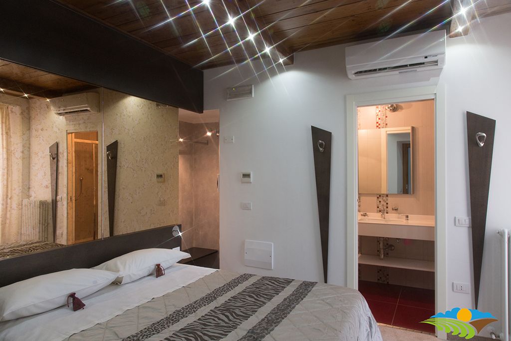 A bedroom with a large bed, a mirror, and a bathroom visible through an open door.