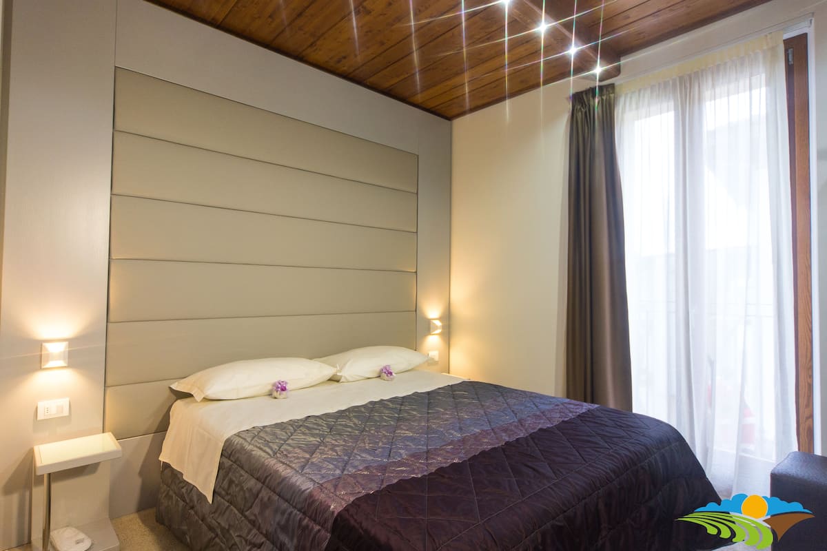 Een slaapkamer met een bed, nachtlampjes, een hoofdeinde en een raam met gordijnen.