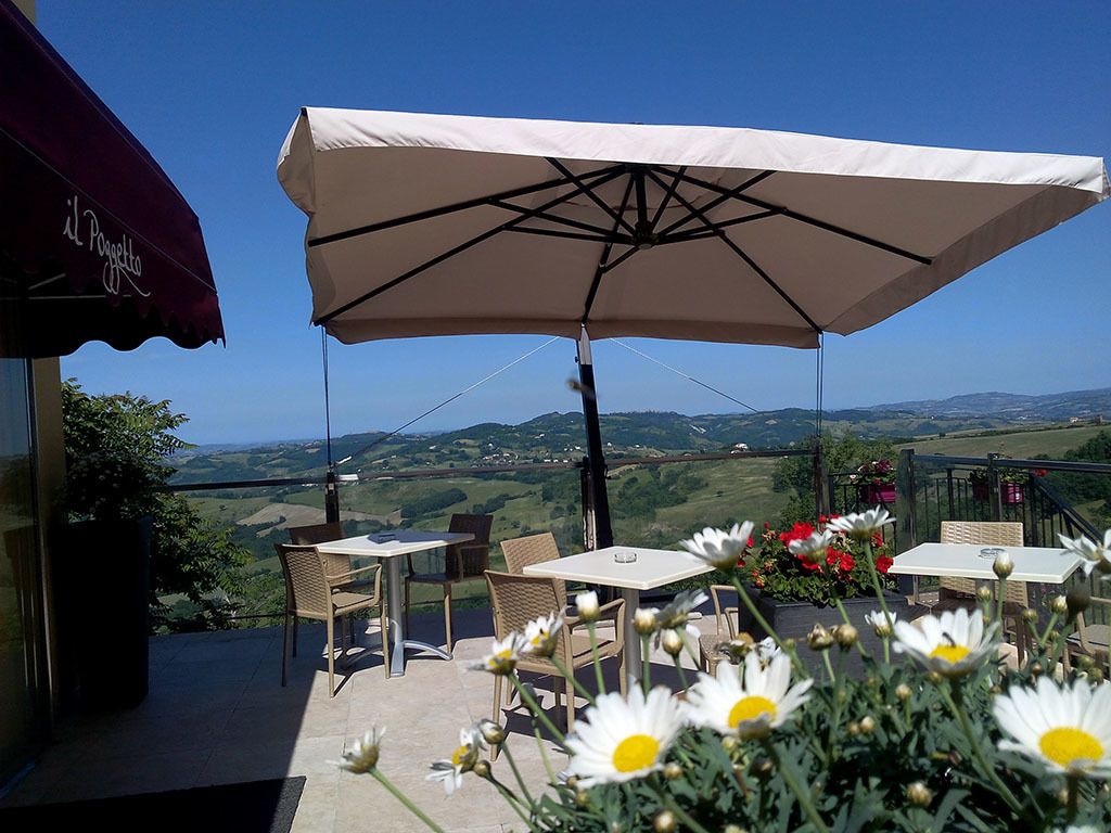 Eine Terrassensitzgruppe mit Tischen und Stühlen, einem großen Sonnenschirm und Blick auf die Landschaft.