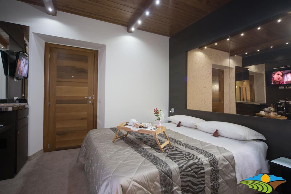 Een hotelkamer met een bed, een houten deur, een nachtkastje met dienblad, een spiegel en een televisie.