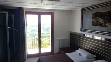 A hotel room with two beds, a large window with a view, a radiator, and a painting on the wall.