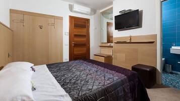 A bedroom with a bed, a television, a mirror, a wardrobe, and a bathroom with blue tiles.