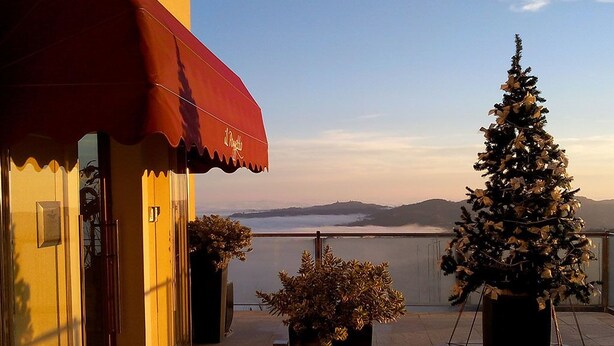 A balcony with a view of a body of water and mountains, a Christmas tree, and a red awning. - IL POGGETTO DI MERLI SILVIA & C. SAS (Tavoleto)