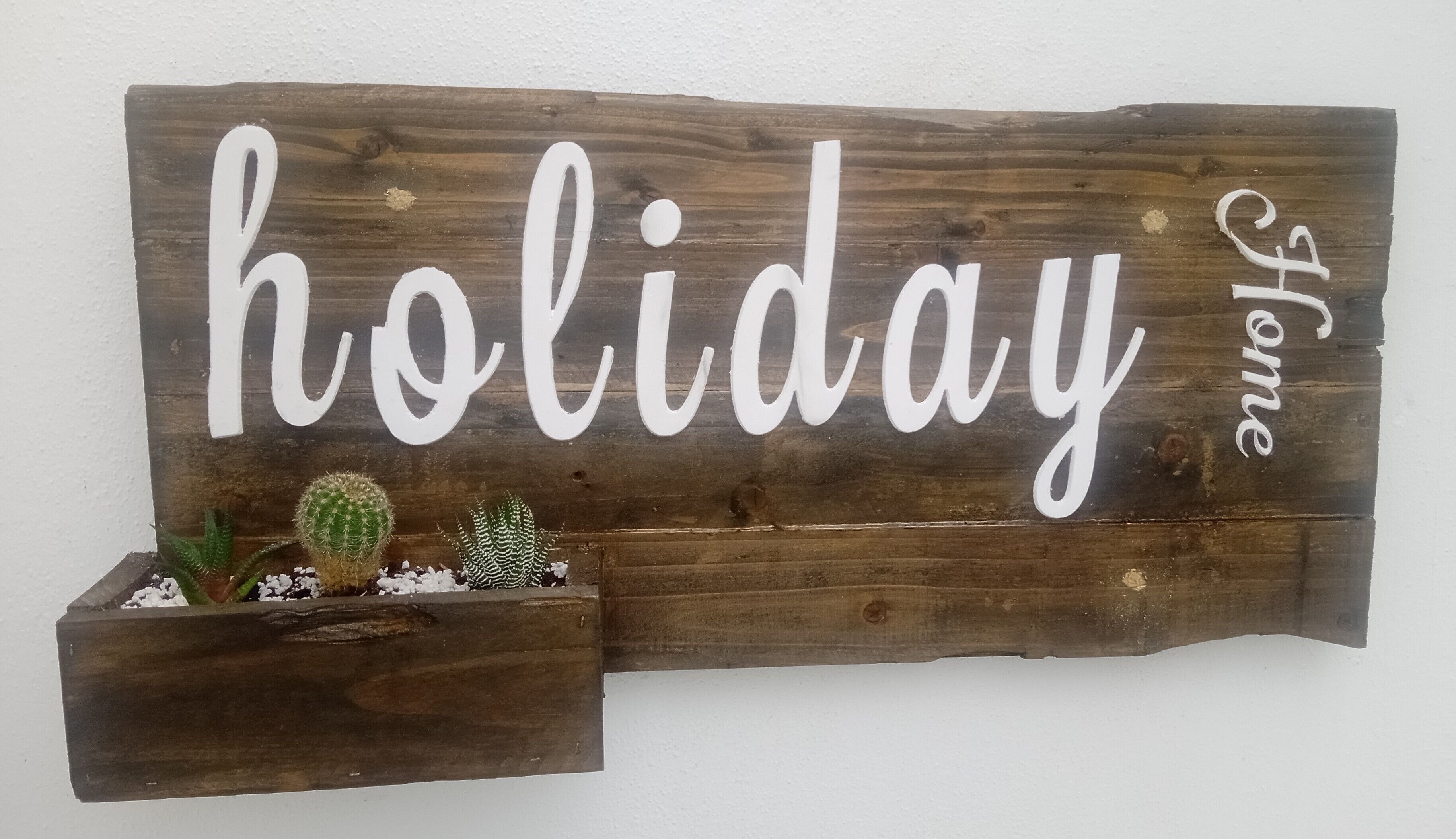 A wooden sign with the words "holiday home" and a small planter with cacti.