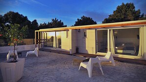 Patio esterno moderno con zona salotto, un piccolo albero e un edificio con ampie vetrate.