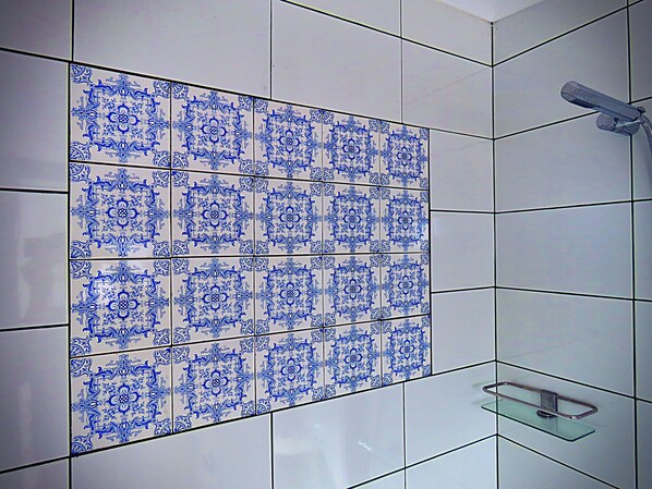 Un baño con azulejos blancos y motivos decorativos azules, cabina de ducha de vidrio y un perchero de metal.