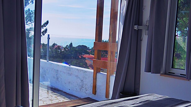 Una camera da letto con un'ampia porta finestra scorrevole che dà su un balcone, un letto con copripiumino fantasia e una sedia sul balcone.