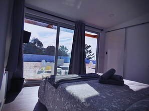 A bedroom with a large window, a bed with a patterned bedspread, and a view of the outside. - Residencia Praia Norte - AL (Nazaré)