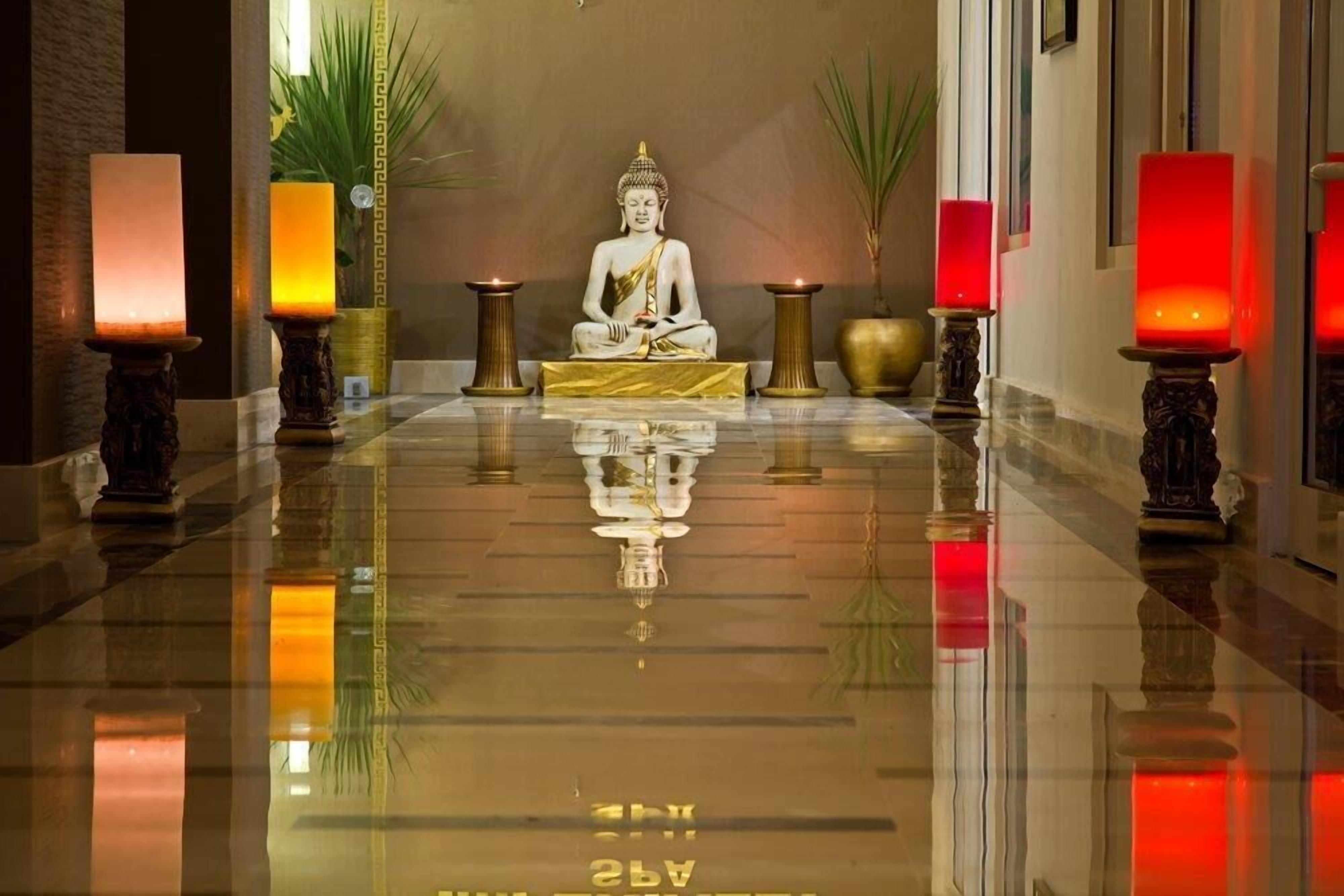 Une statue de Bouddha dans un couloir aux murs réfléchissants, décoré de bougies et de plantes.