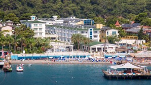 Ein Küstenhotel mit mehreren Gebäuden, einem Strandbereich inklusive Liegestühlen und einem Steg.