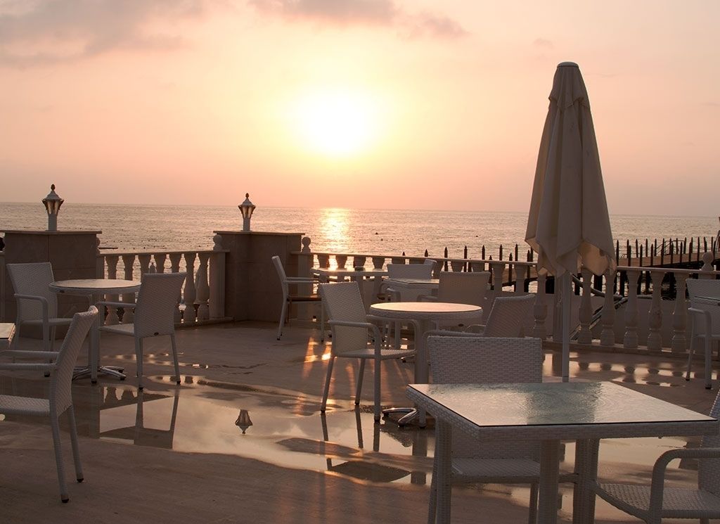 An outdoor seating area with tables and chairs, overlooking the sea during sunset.