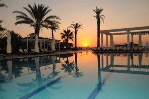 A poolside area with lounge chairs and palm trees during sunset. - Onkel Resort Hotel (Kemer)