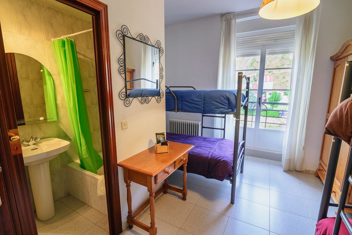 Une petite pièce comprenant un lit superposé, un bureau en bois, un miroir, un lavabo et une fenêtre donnant sur l’extérieur.