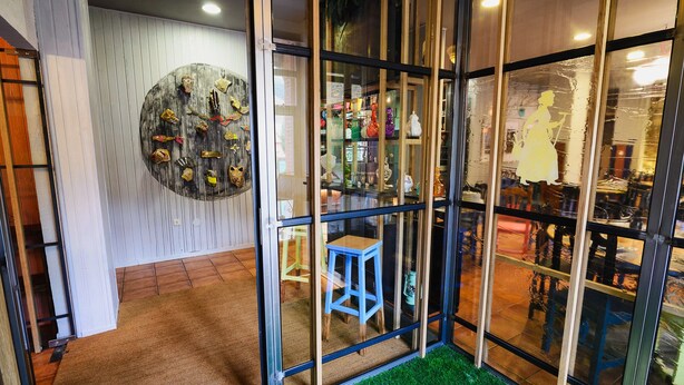 A room with a glass partition, a blue stool, and a wall with various decorative items. - Albergue Cueva de Valporquero (Vegacervera)
