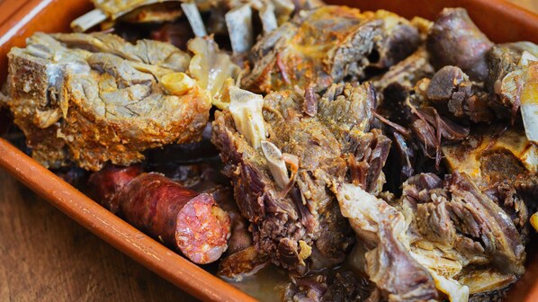 A ceramic dish containing various types of meat, including sausages and possibly pork.