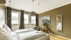 A hotel room with a large bed, a chair, a small table with a plant, a painting on the wall, and a window with curtains. - Five Reasons Hotel & Hostel (Nuremberg)