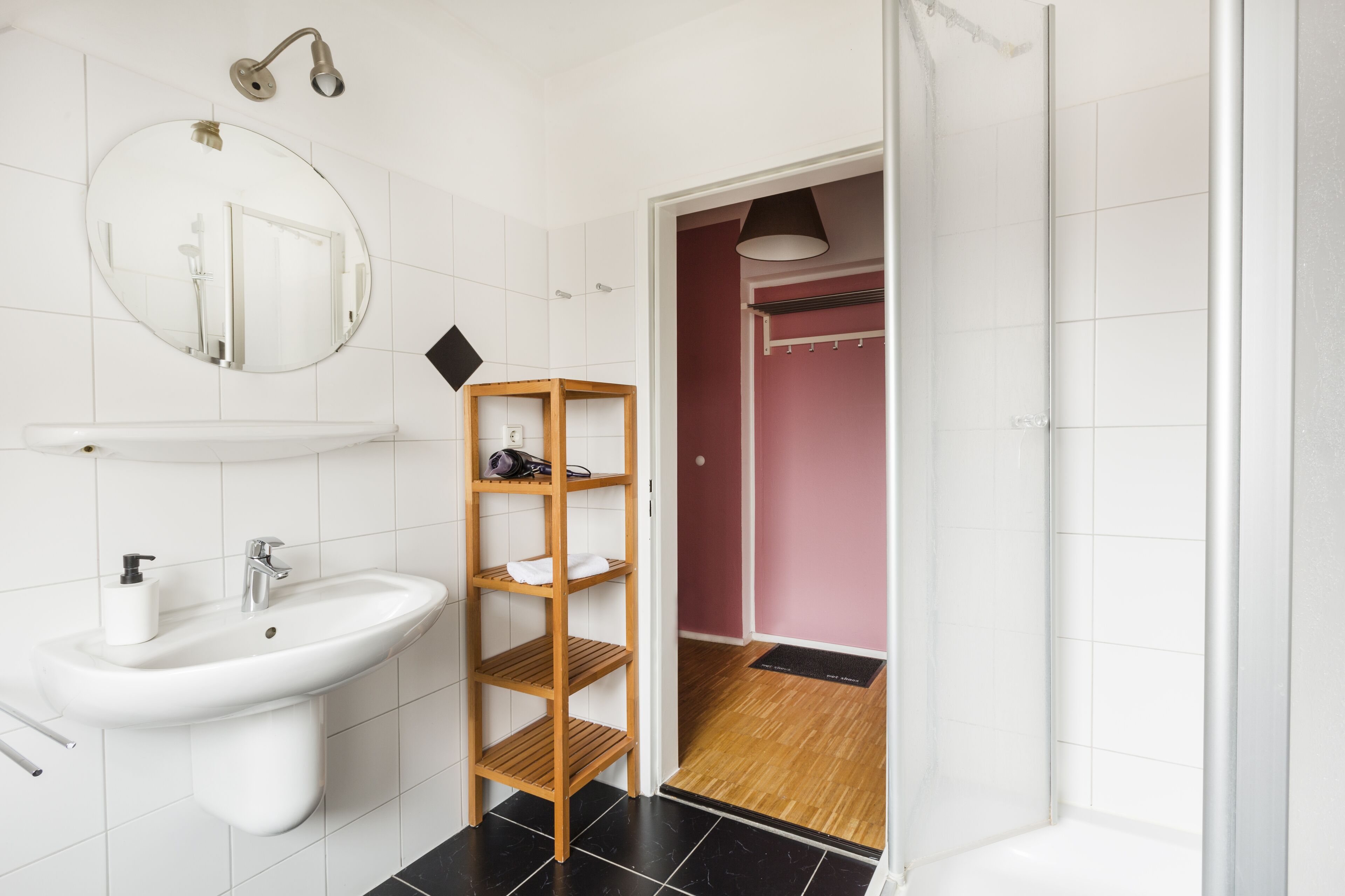 A bathroom with a white sink, a mirror, and a wooden shelf.