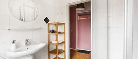 A bathroom with a white sink, a mirror, and a wooden shelf.