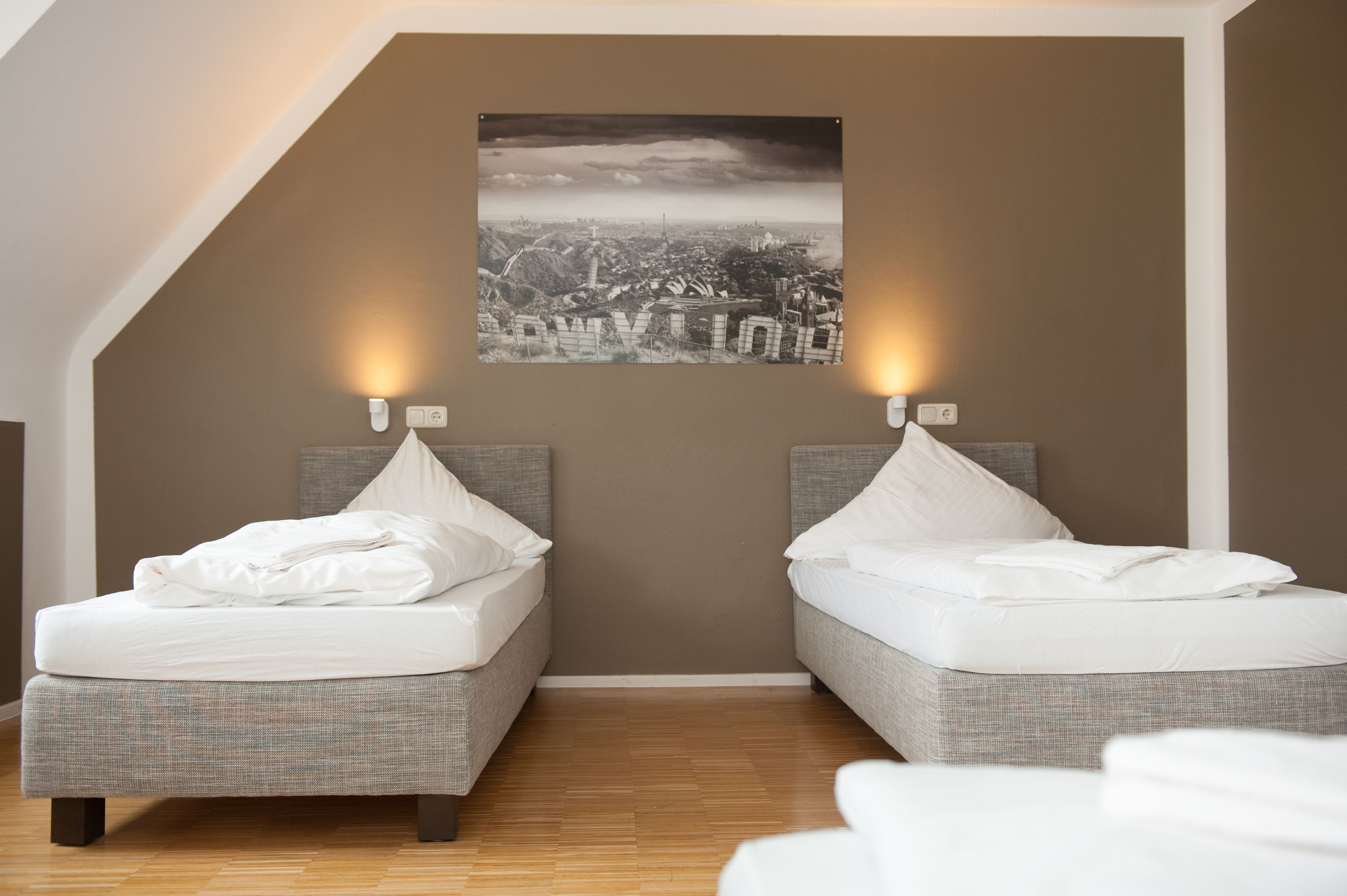 A bedroom with two beds, a cityscape view, and a sloped ceiling.