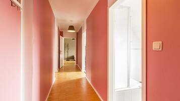 A hallway with pink walls and wooden flooring leading to a bathroom with a glass shower.