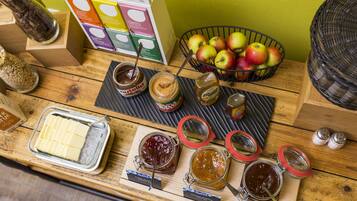 A wooden table with jars of spreads, a bowl of apples, and a box of Charitea products.