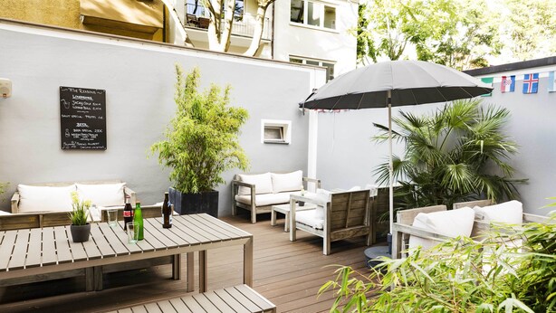An outdoor patio with wooden furniture, a table with bottles, and a sign listing food and drink specials. - Five Reasons Hotel & Hostel (Nuremberg)