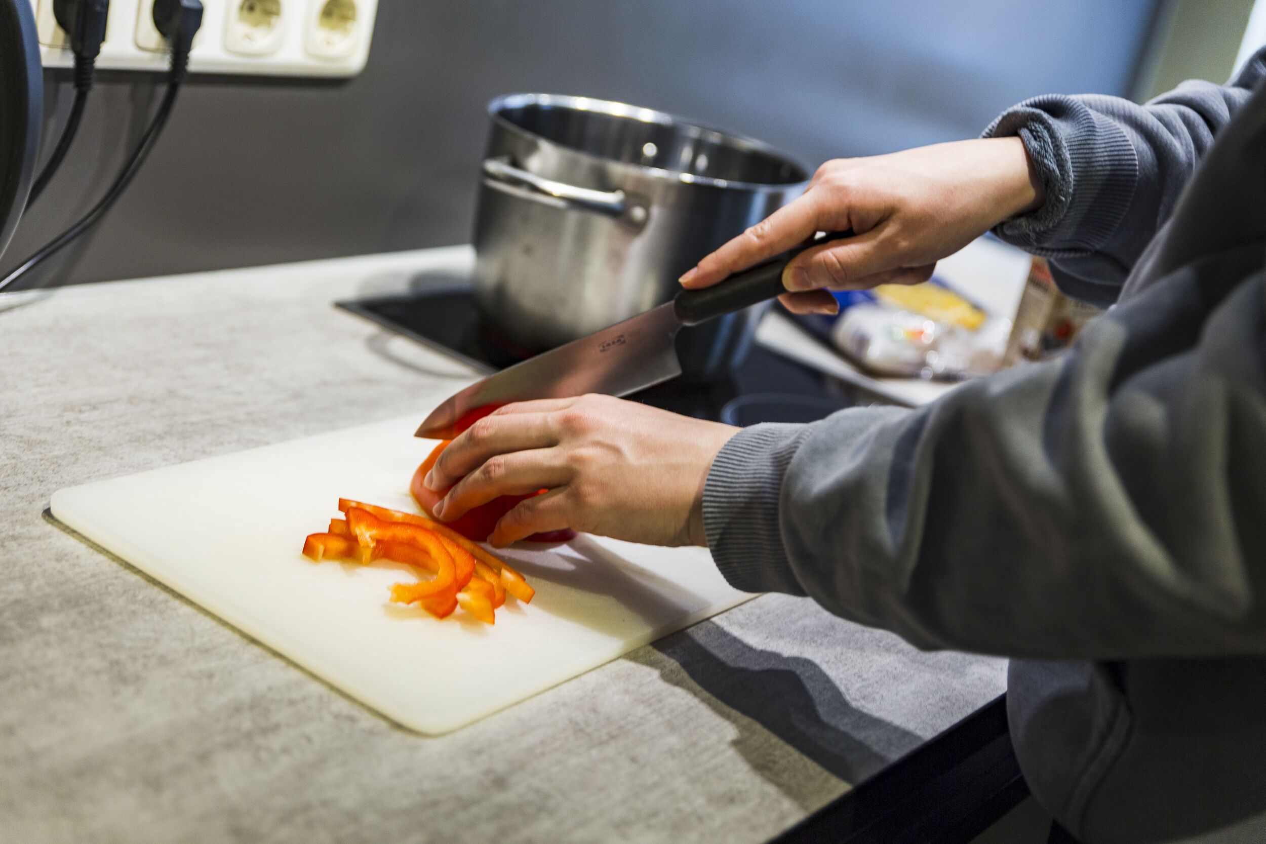 Una persona picando verduras sobre una tabla de cortar blanca.