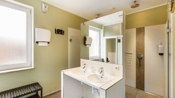 A bathroom with two sinks, a bench, and a shower.