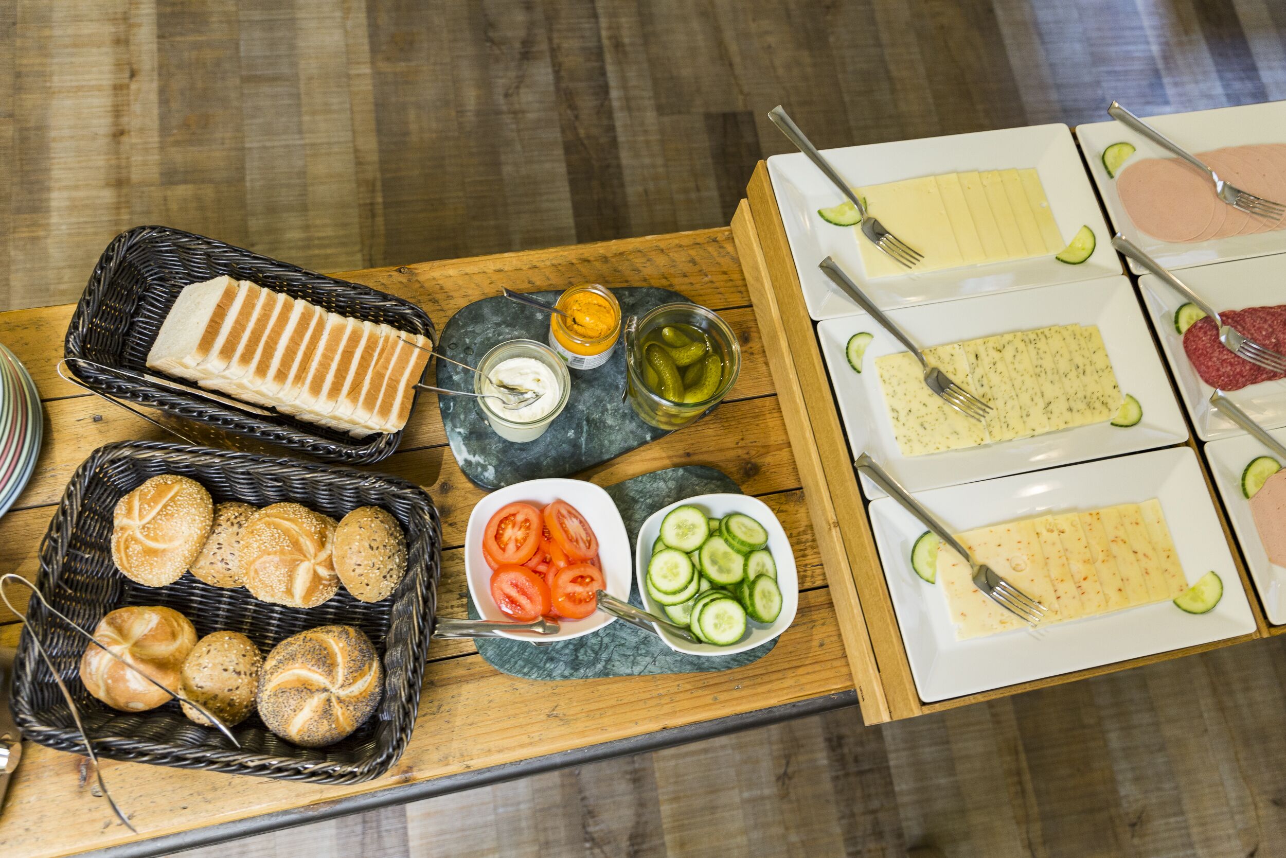 A buffet table with various food items including bread, sliced tomatoes, cucumbers, and different types of cheese.