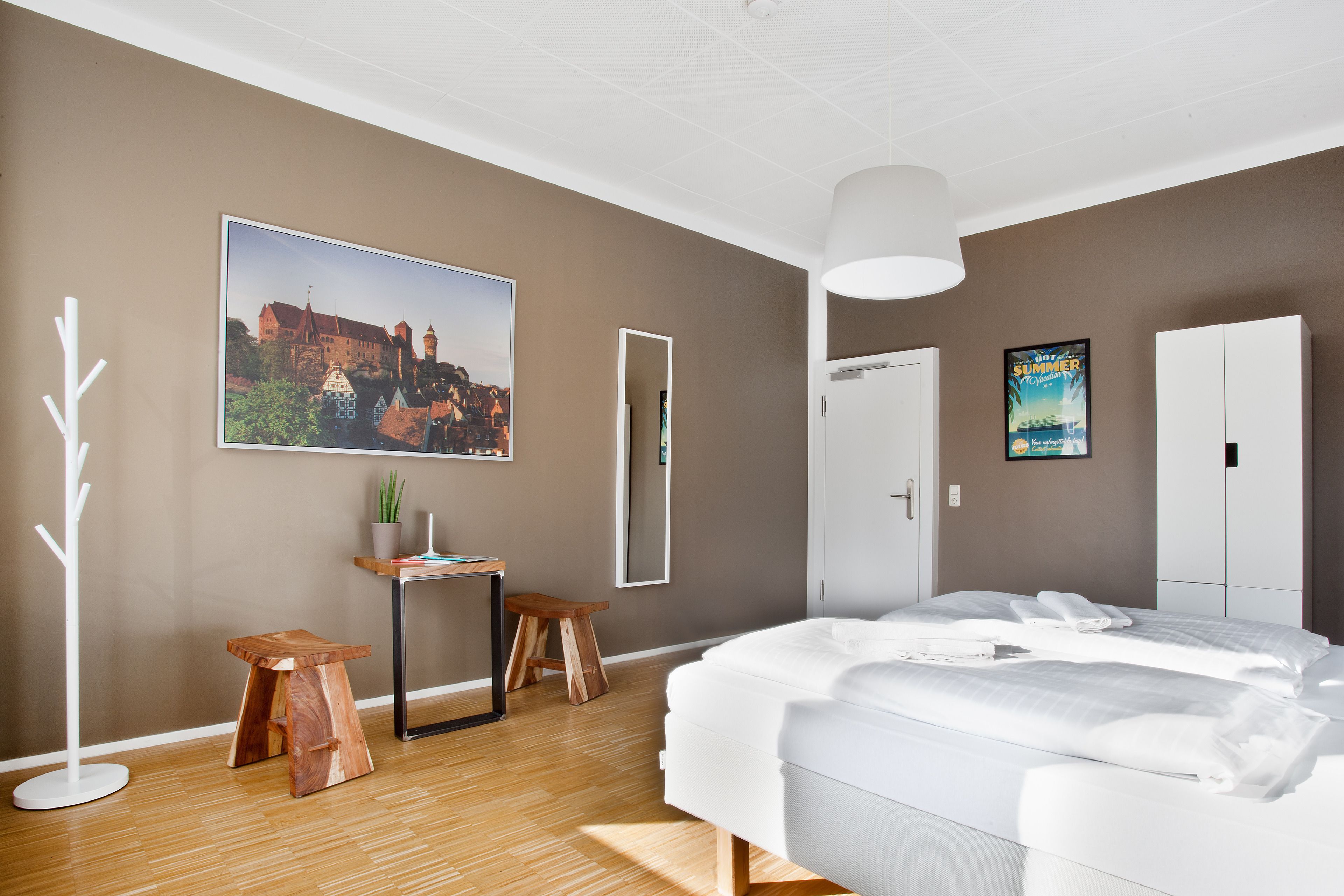 A modern bedroom with a large bed, a desk, two stools, a potted plant, and a framed picture on the wall.