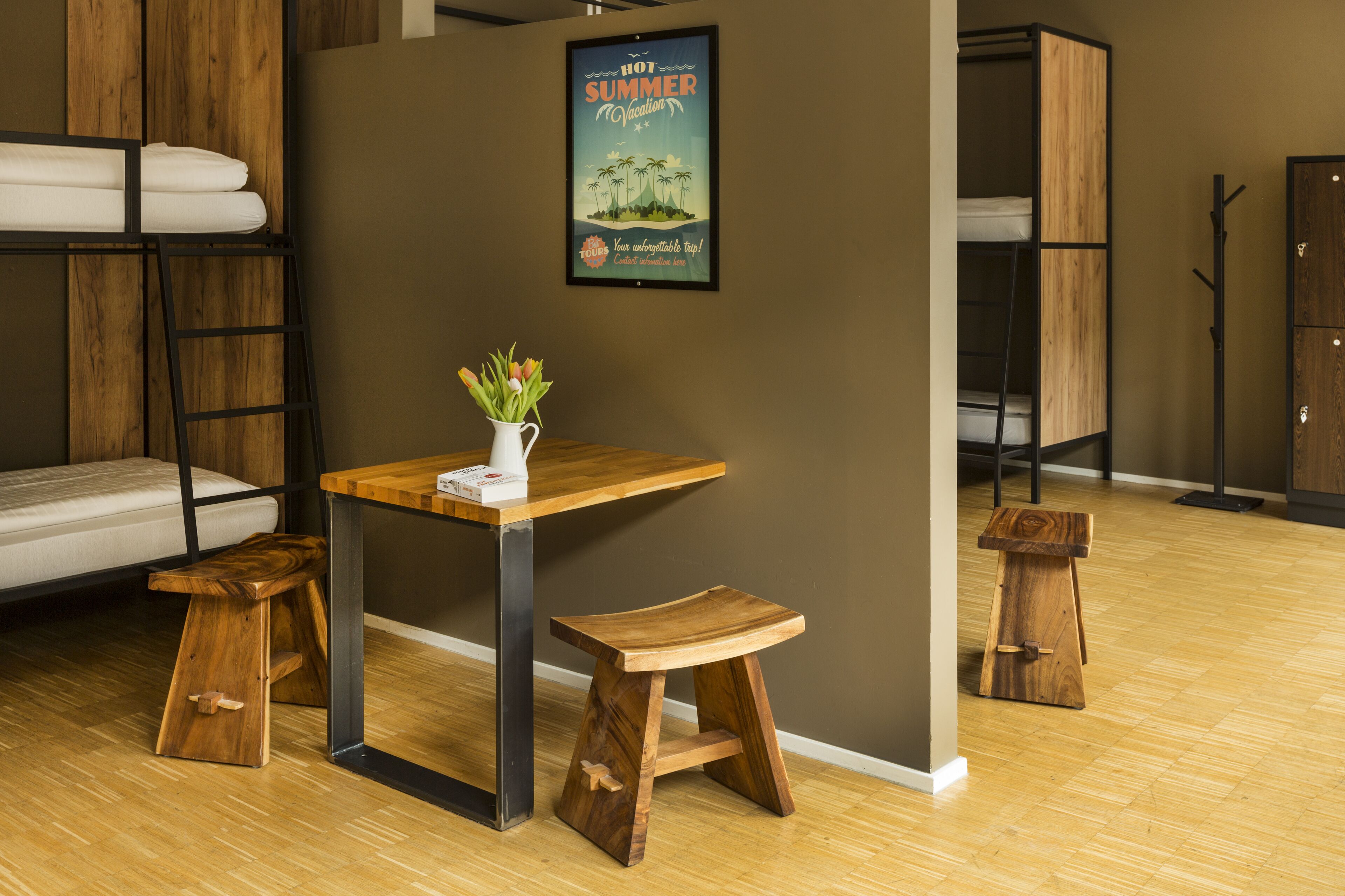 Una habitación con una cama individual superpuesta, una mesa de madera con un florero y dos taburetes.