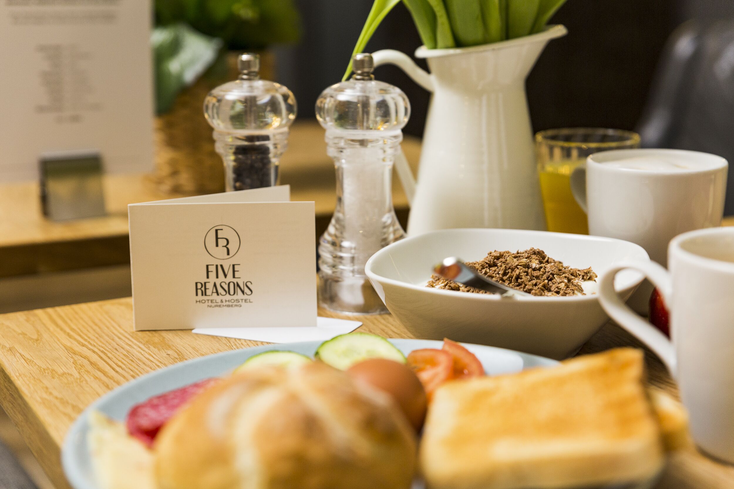 Un desayuno con un cartel que dice "Five Reasons Hotel & Hostel", un bol de granola, un plato con tostadas y fruta, una jarra y un salero y pimentero.