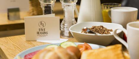 A breakfast setting with a sign reading "Five Reasons Hotel & Hostel", a bowl of granola, a plate with toast and fruit, a pitcher, and a salt and pepper shaker.