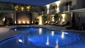 Una piscina de diseño curvo, rodeada de sillones y sombrillas, con un edificio con balcones al fondo.