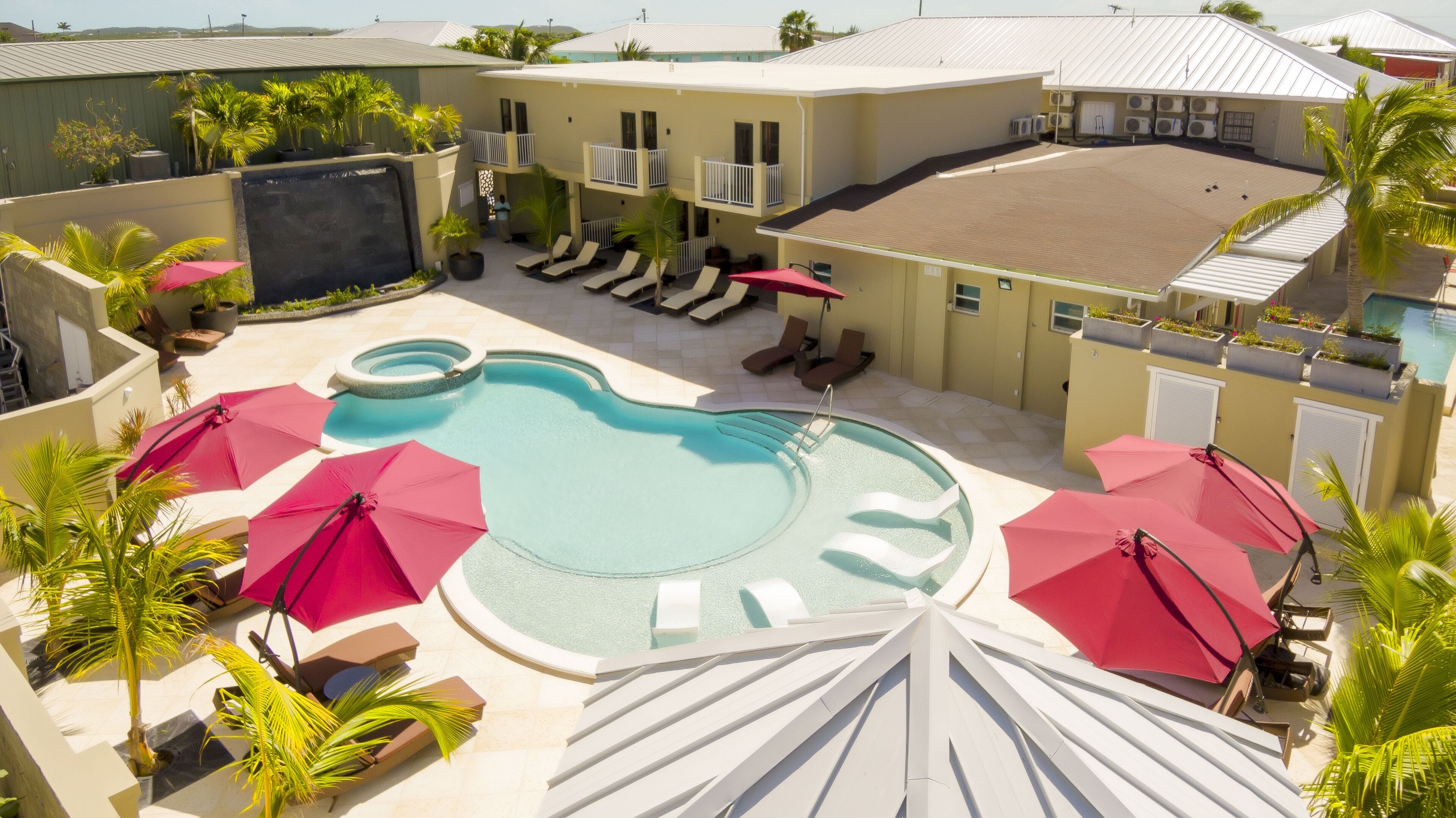 A pool area with multiple lounge chairs and umbrellas, surrounded by buildings with balconies and a pool.