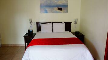 A neatly made bed with white and red bedding, a painting of a boat on water above it, and two bedside tables with lamps.