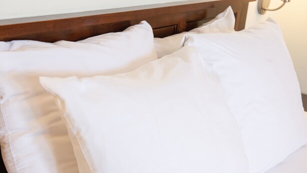 Una cama con ropa de cama blanca y cabecera de madera.