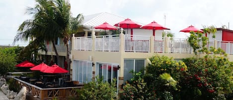 A two-story building with a balcony, red umbrellas, and outdoor seating.