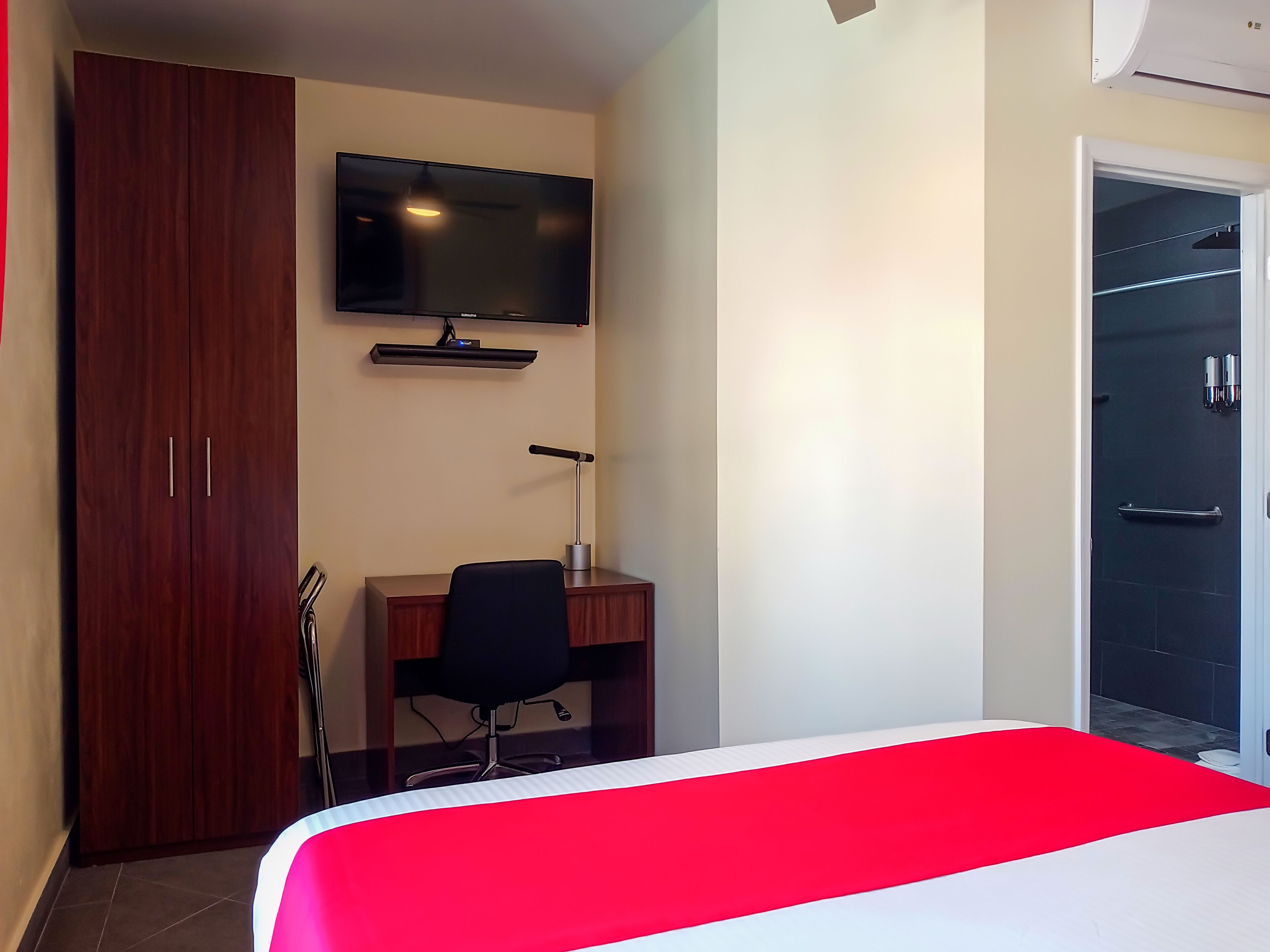 A hotel room with a bed, a desk, a chair, a TV, and a wardrobe.