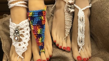 A mannequin with multiple feet adorned with various types of footwear, including crocheted sandals and a colorful beaded anklet.