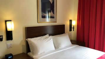 A hotel room with a bed, two bedside lamps, a clock, and a painting on the wall.
