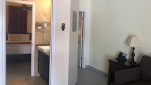 Una habitación de hotel con una cama, un baño con lavabo y teléfono, y una mesita con lámpara.