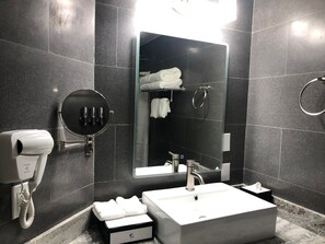 Une salle de bain moderne avec un grand miroir, un lavabo blanc, un porte-serviettes et un sèche-cheveux.